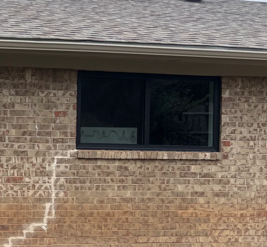 The same rear window after replacement, a black sliding window in tan brick