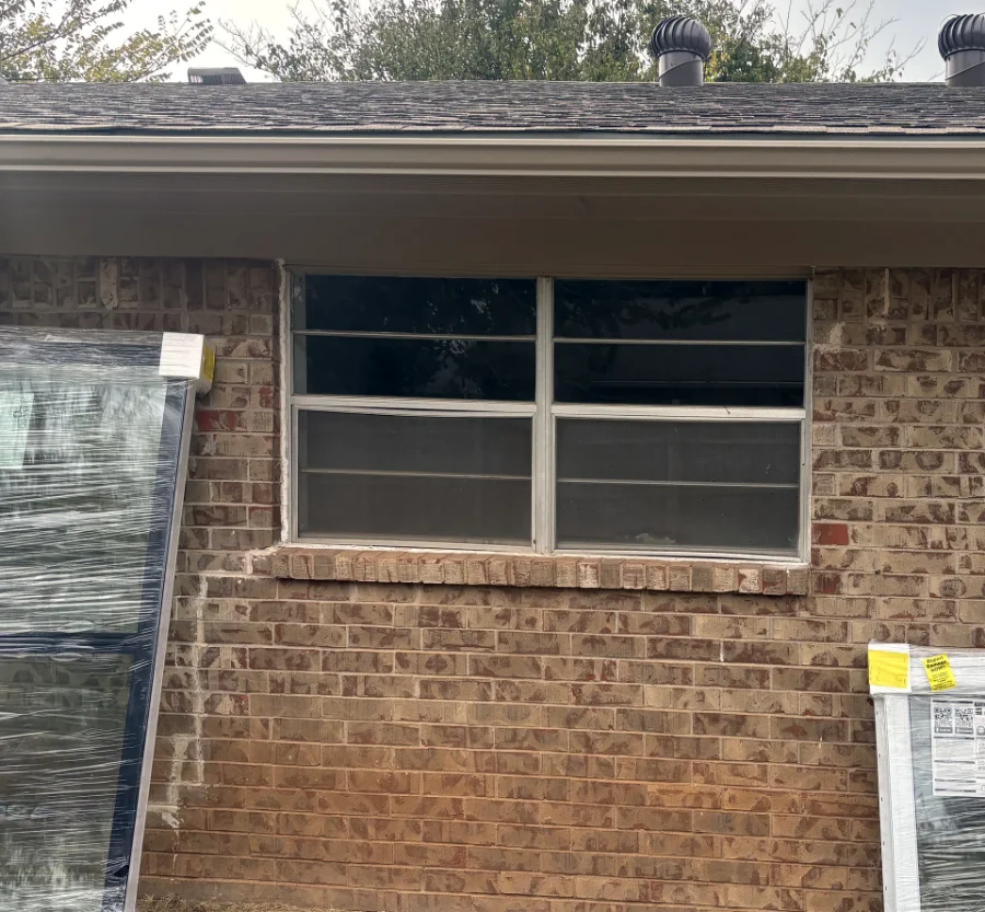 A rear window before replacement, an old window with white frames and screens in tan brick