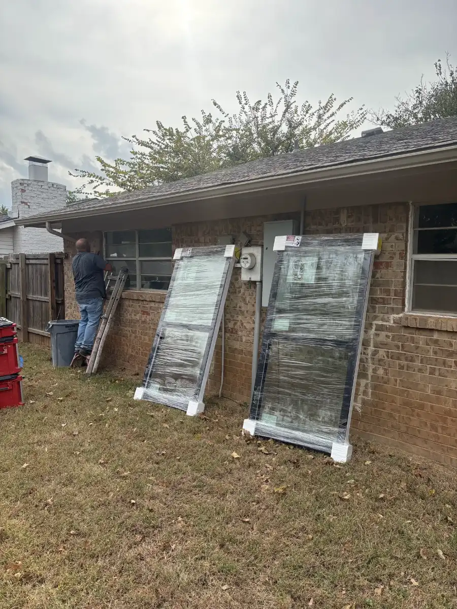 An old window being taken out, with two new wrapped windows leaning on the brick wall