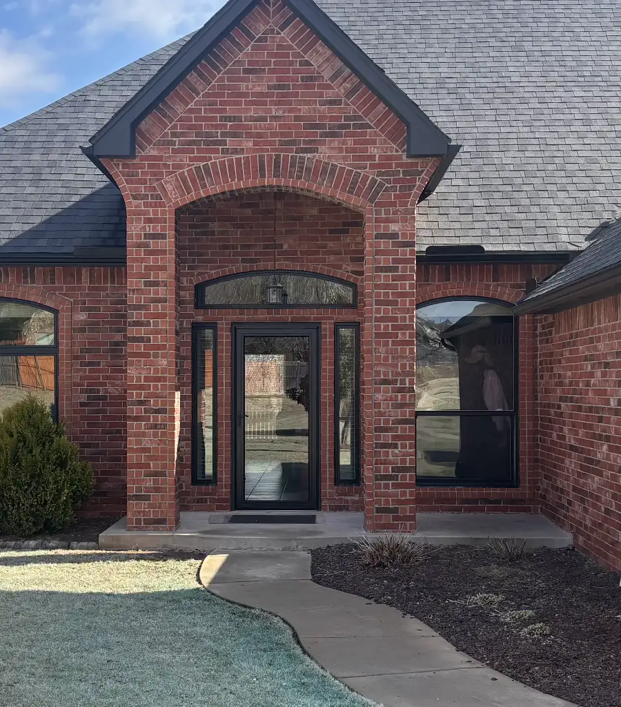 A brick entry with a black glass front door and black-framed sidelights