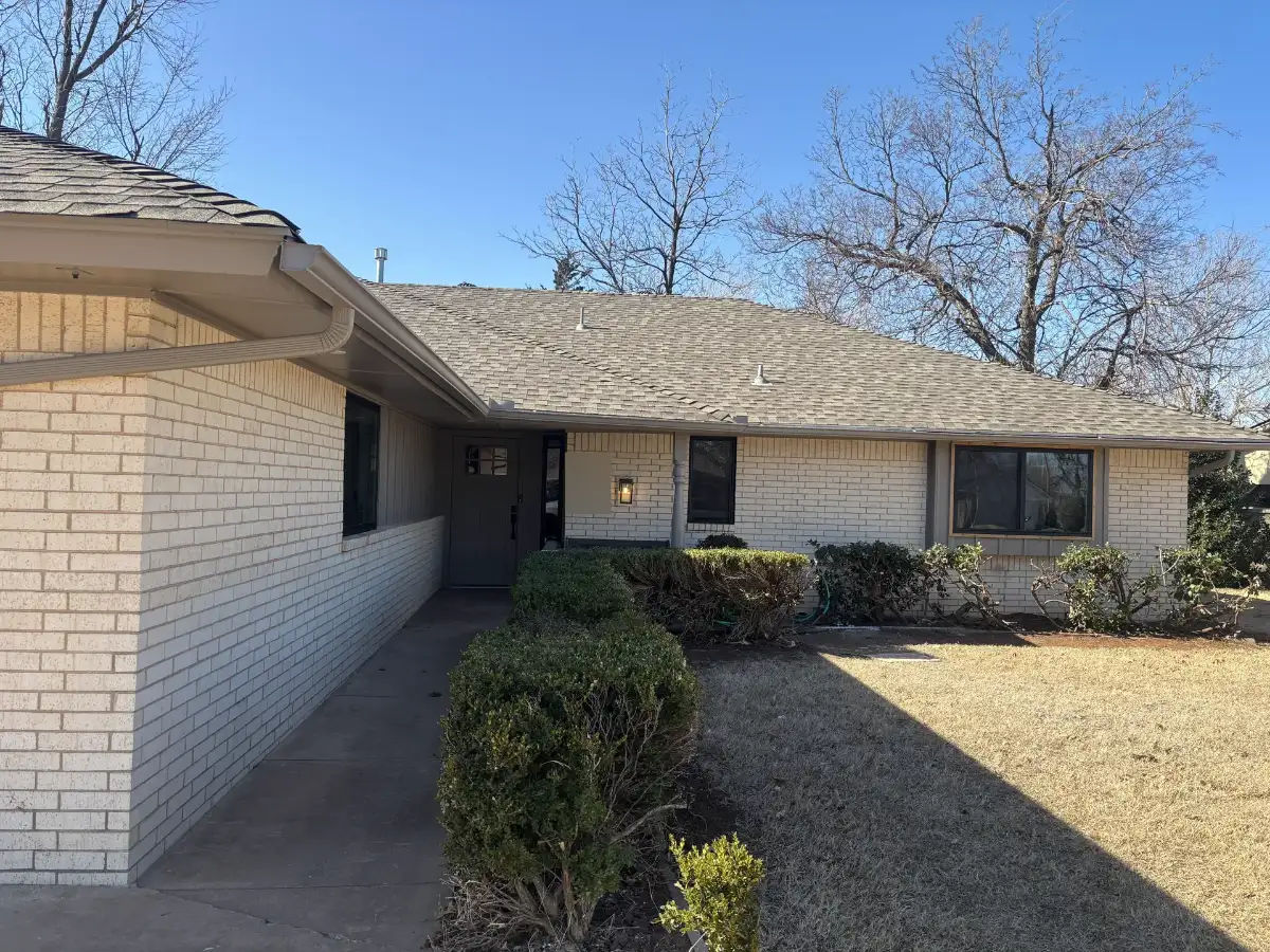 A cream brick ranch house with new dark-framed windows beside its front walk