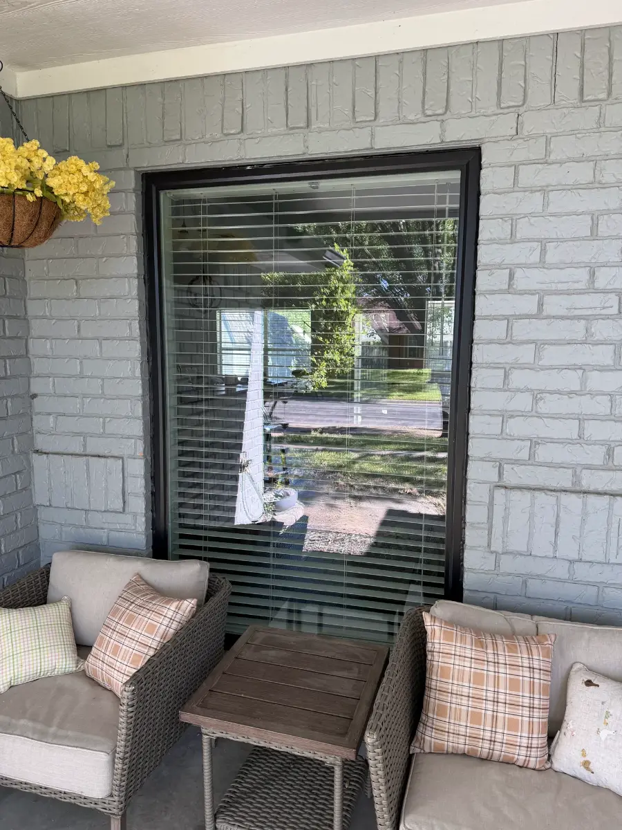 A tall black-framed window in a painted gray brick wall on a covered porch