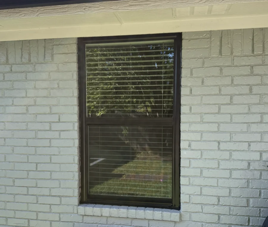 A dark-framed single-hung window with blinds in a painted brick wall